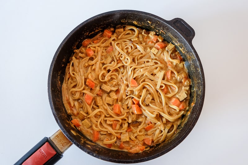 cast iron pan on white table full of coconut curry noodles