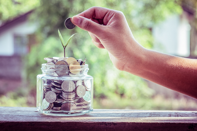 hand placing coins in jar on ledge benefits of frugal living