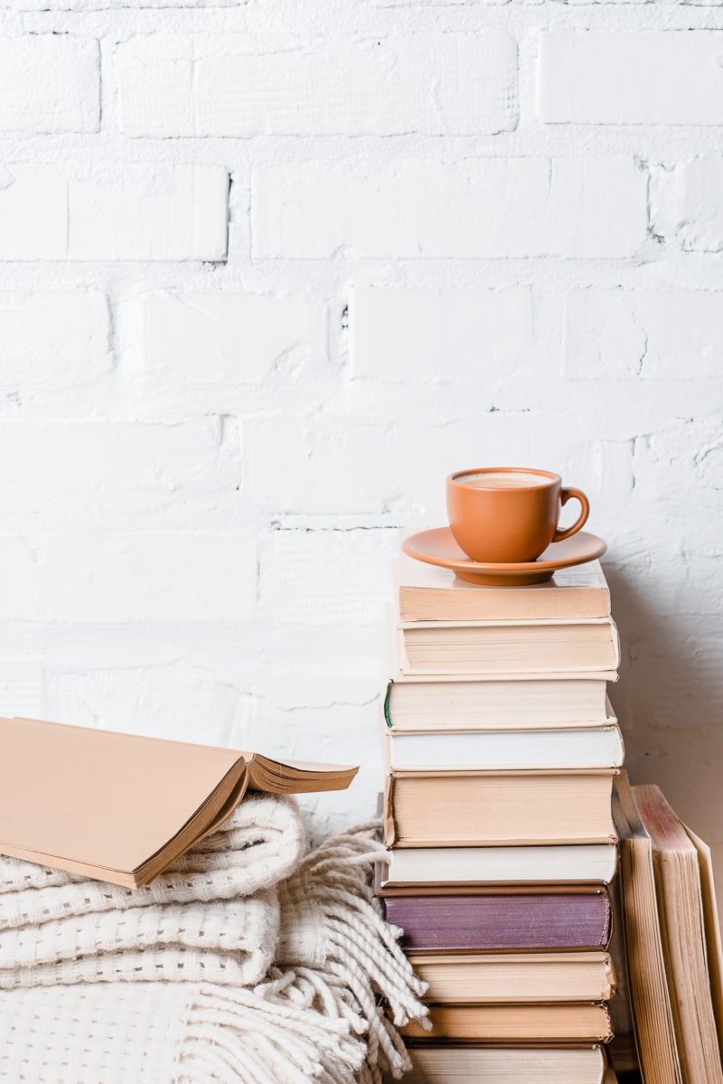 mug and saucer on stack of books beside bed with white brick behind