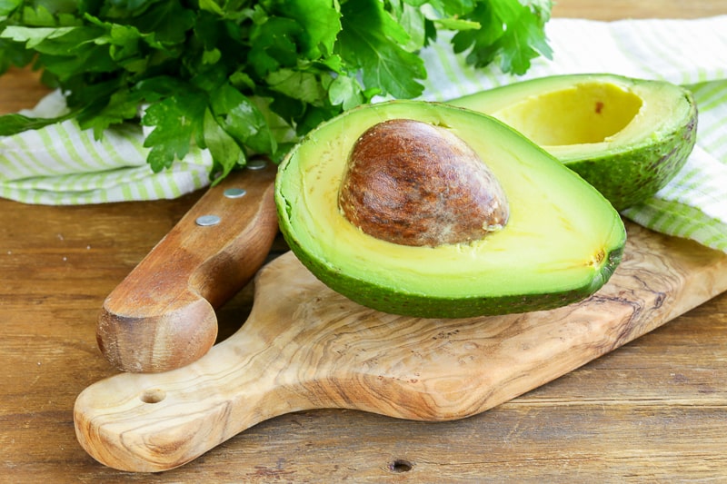 avocado sliced in half on wooden cutting board how to reduce food waste at home